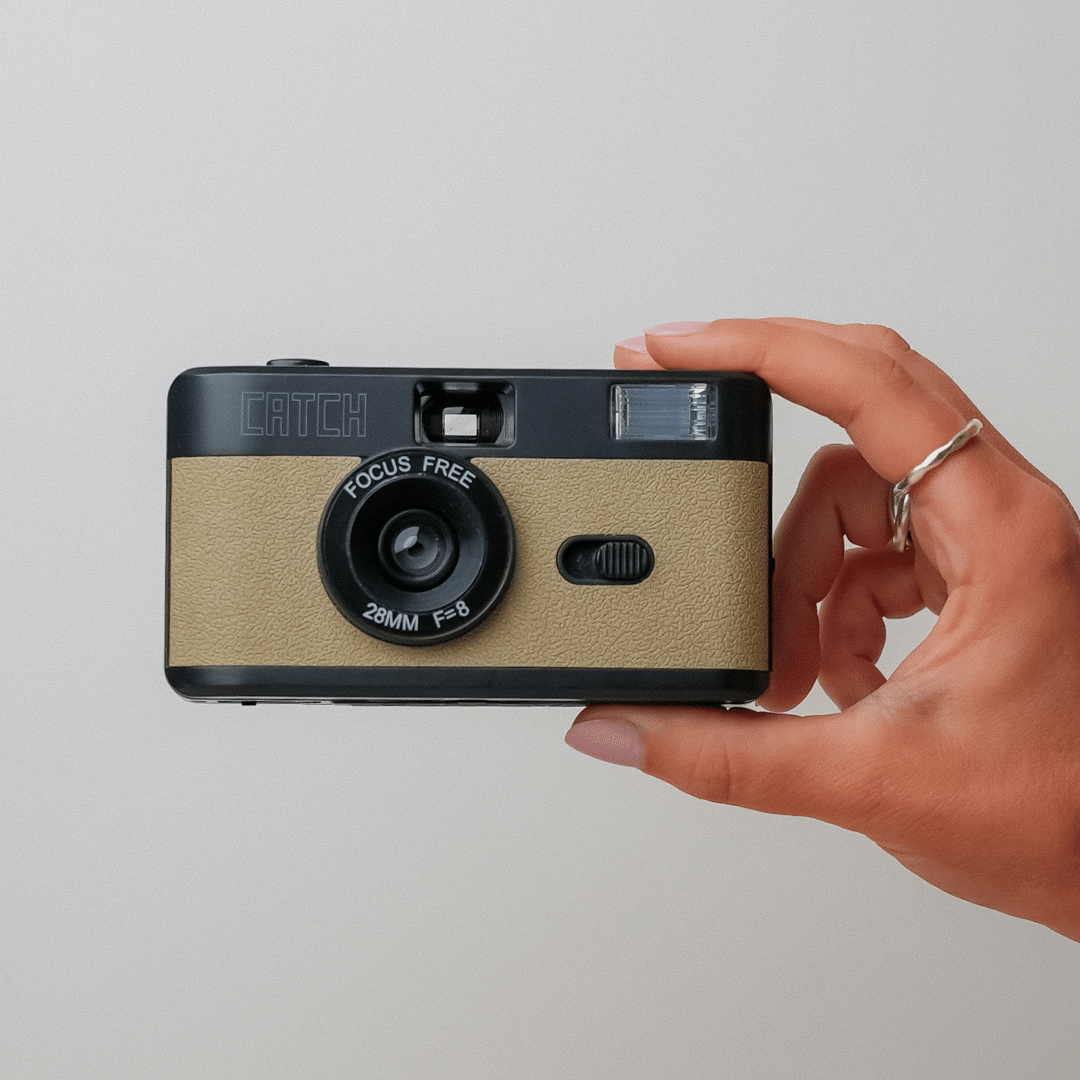 Hand holding a vintage-style camera against a plain background.