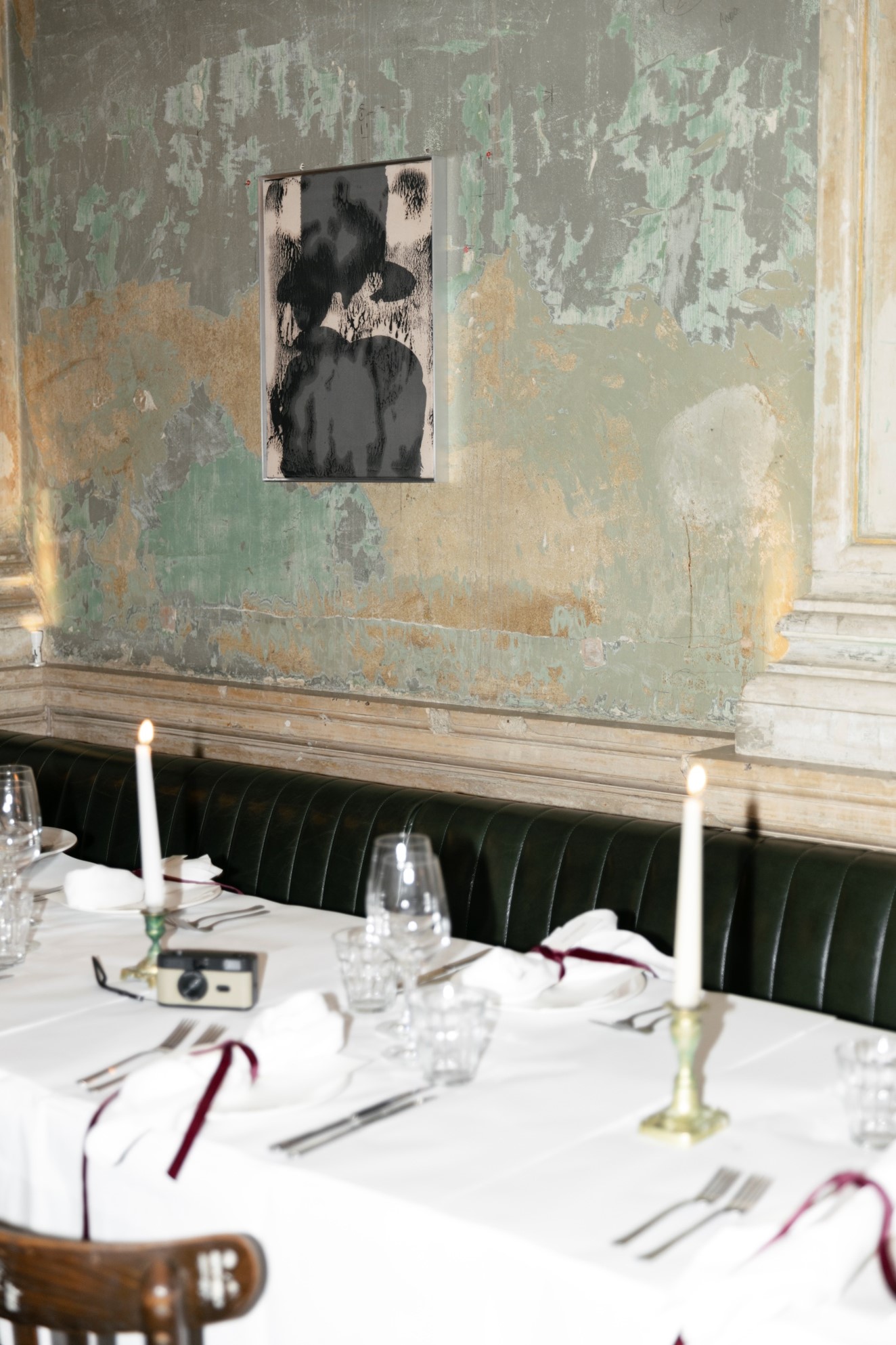 Elegant dining table with candles, glasses, and a vintage camera on a rustic wall background.