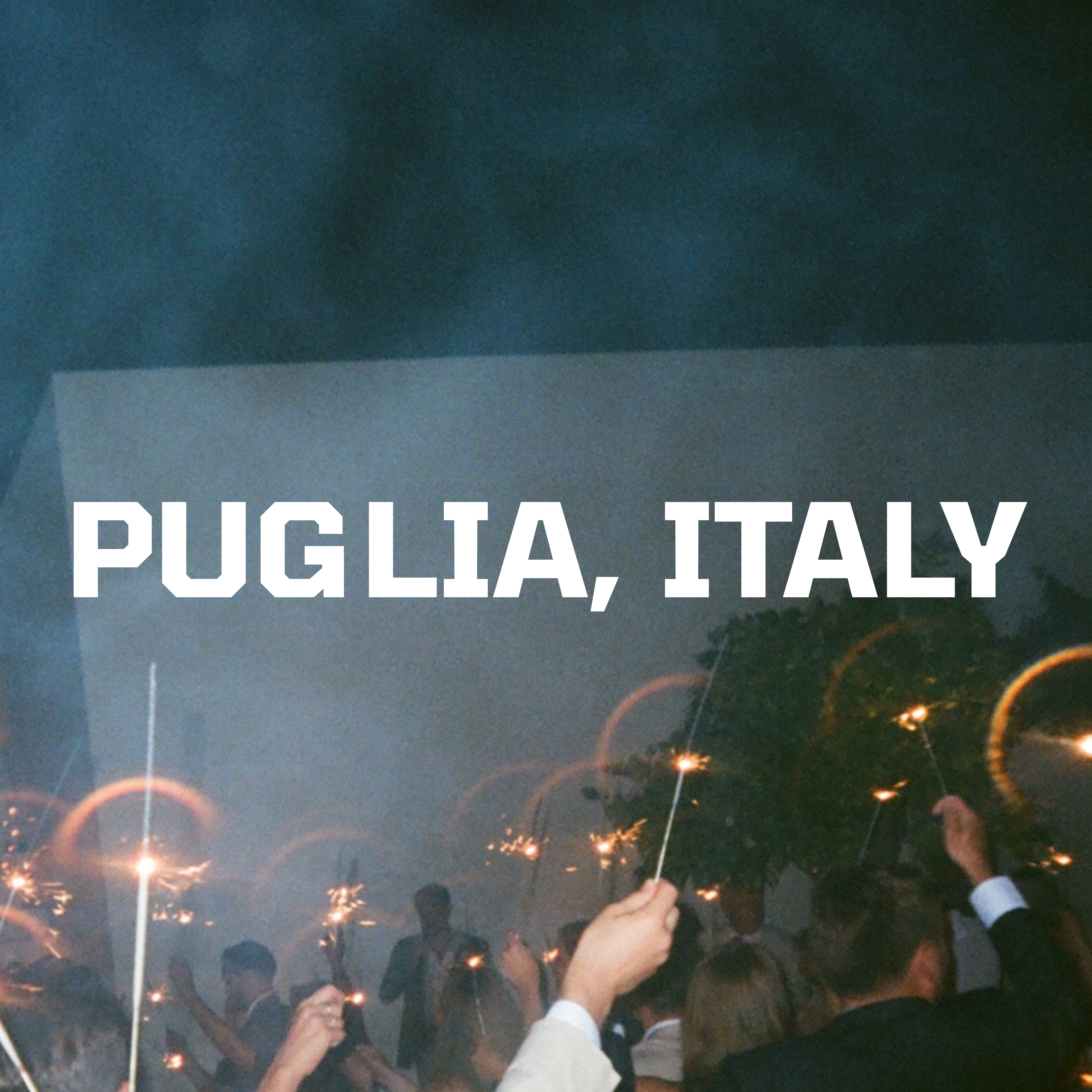 People holding sparklers beneath text 'PUGLIA, ITALY' at night.