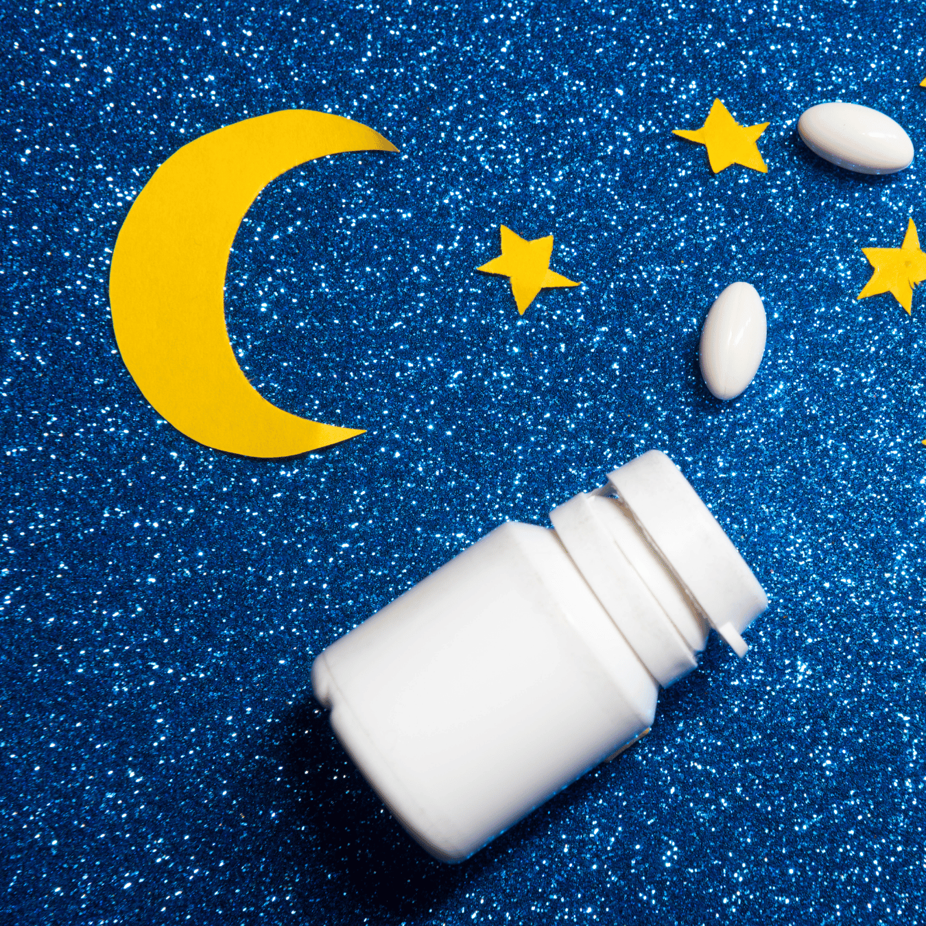 White pill bottle with pills, yellow moon, and stars on blue glitter background.