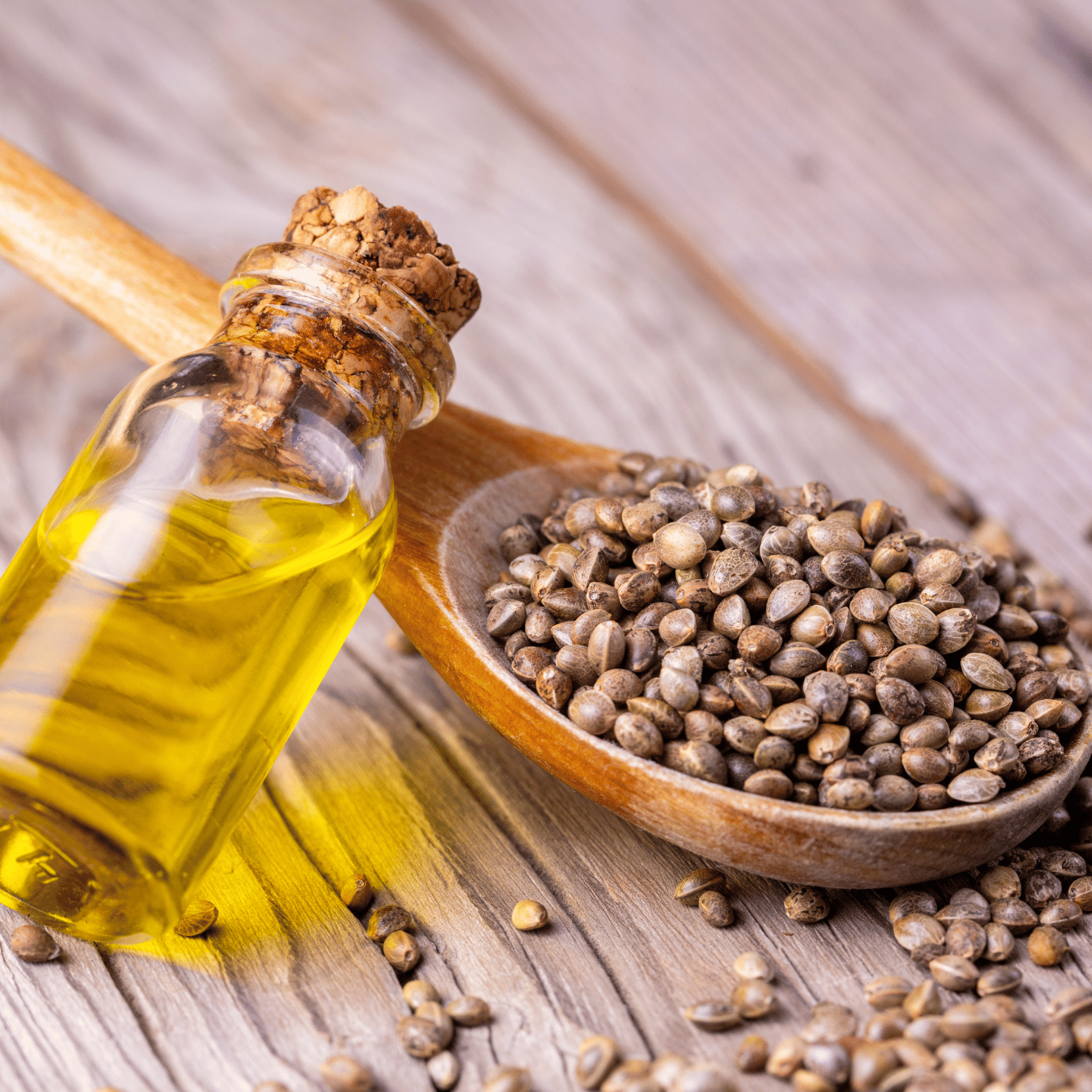 A bottle of oil and a wooden spoon with seeds on a wooden surface.
