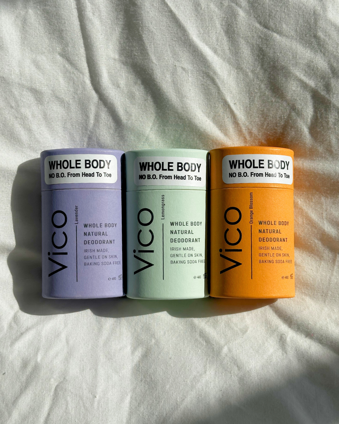 Three tubes of Vico Whole Body Deodorant in purple, green, and orange on a white cloth background.