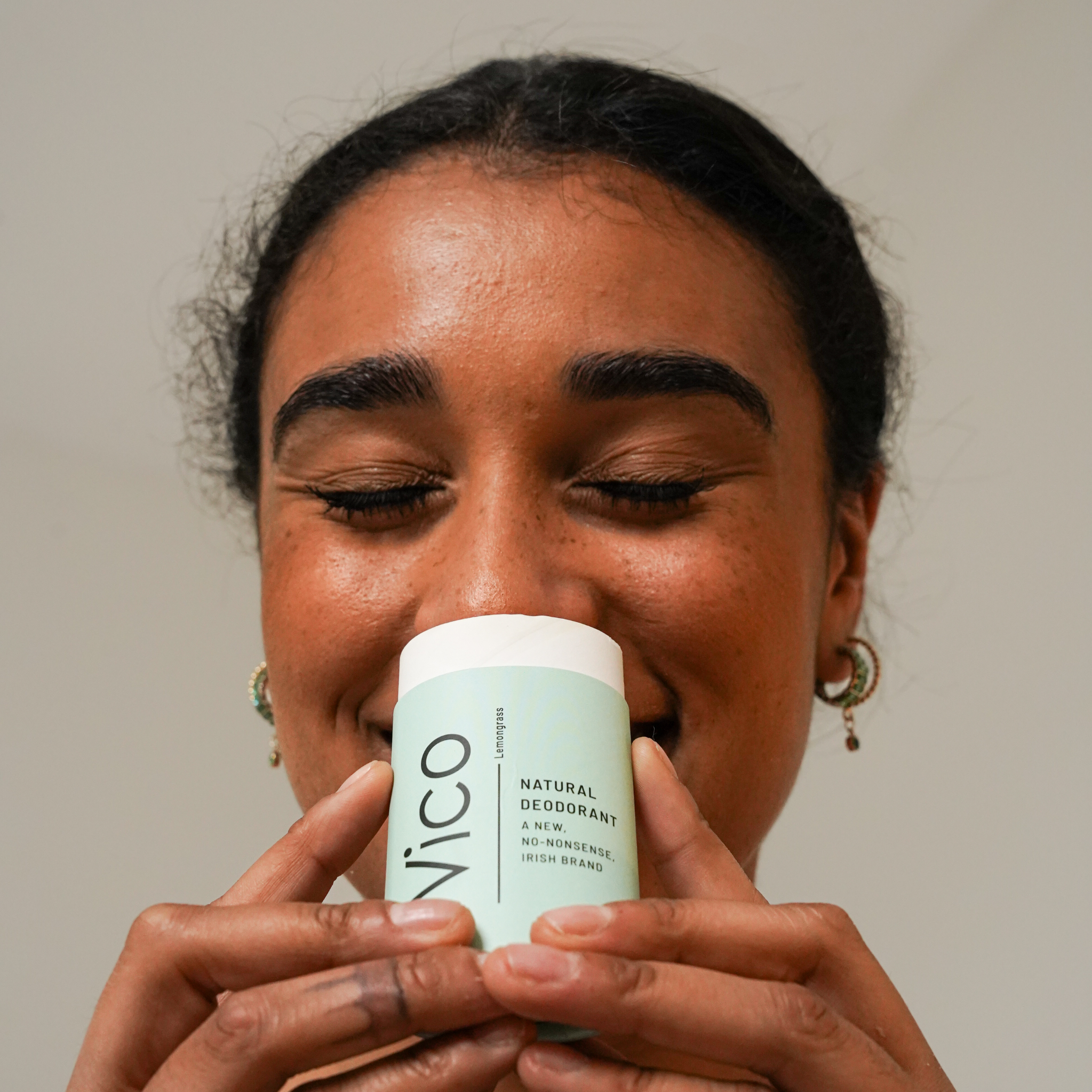 A smiling woman with her eyes closed holds a stick of Vico natural deodorant to her nose.