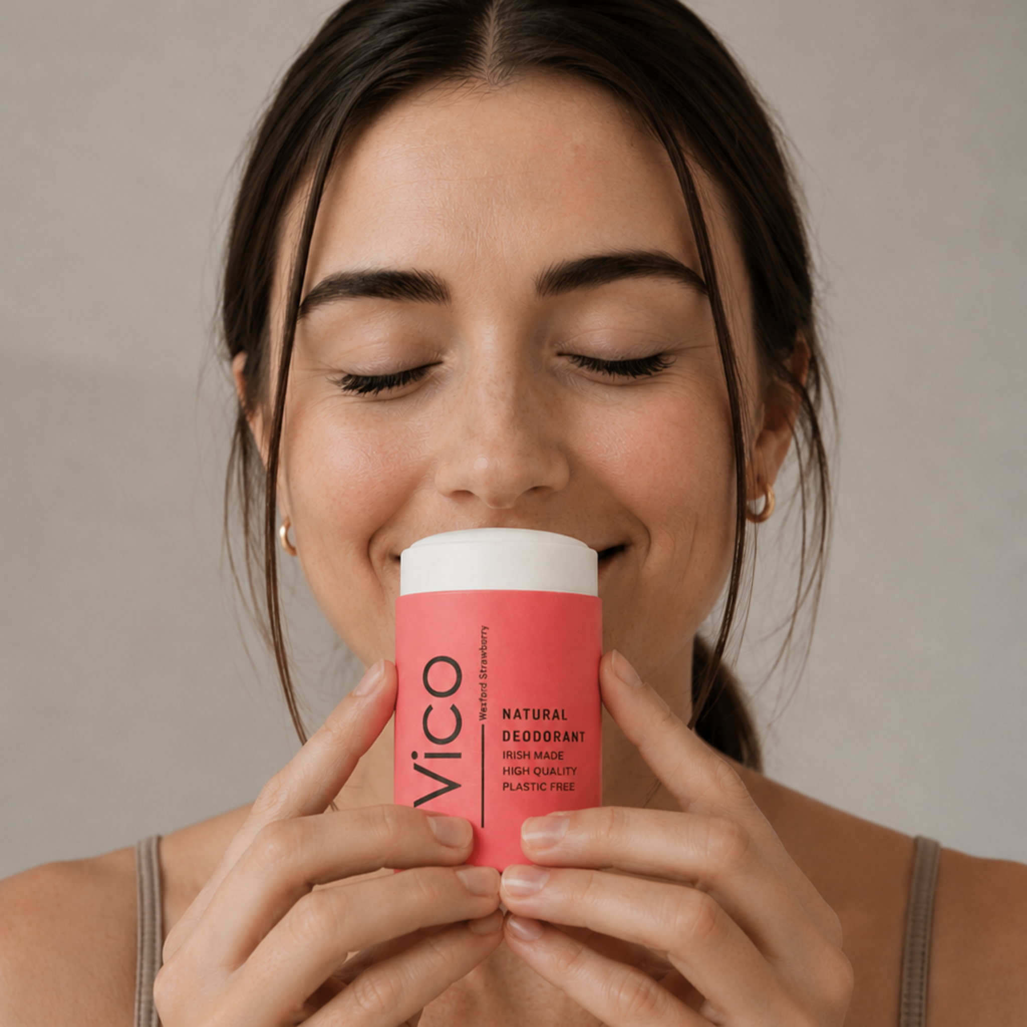 A woman with her eyes closed smiles as she smells a pink stick of Vico natural deodorant.