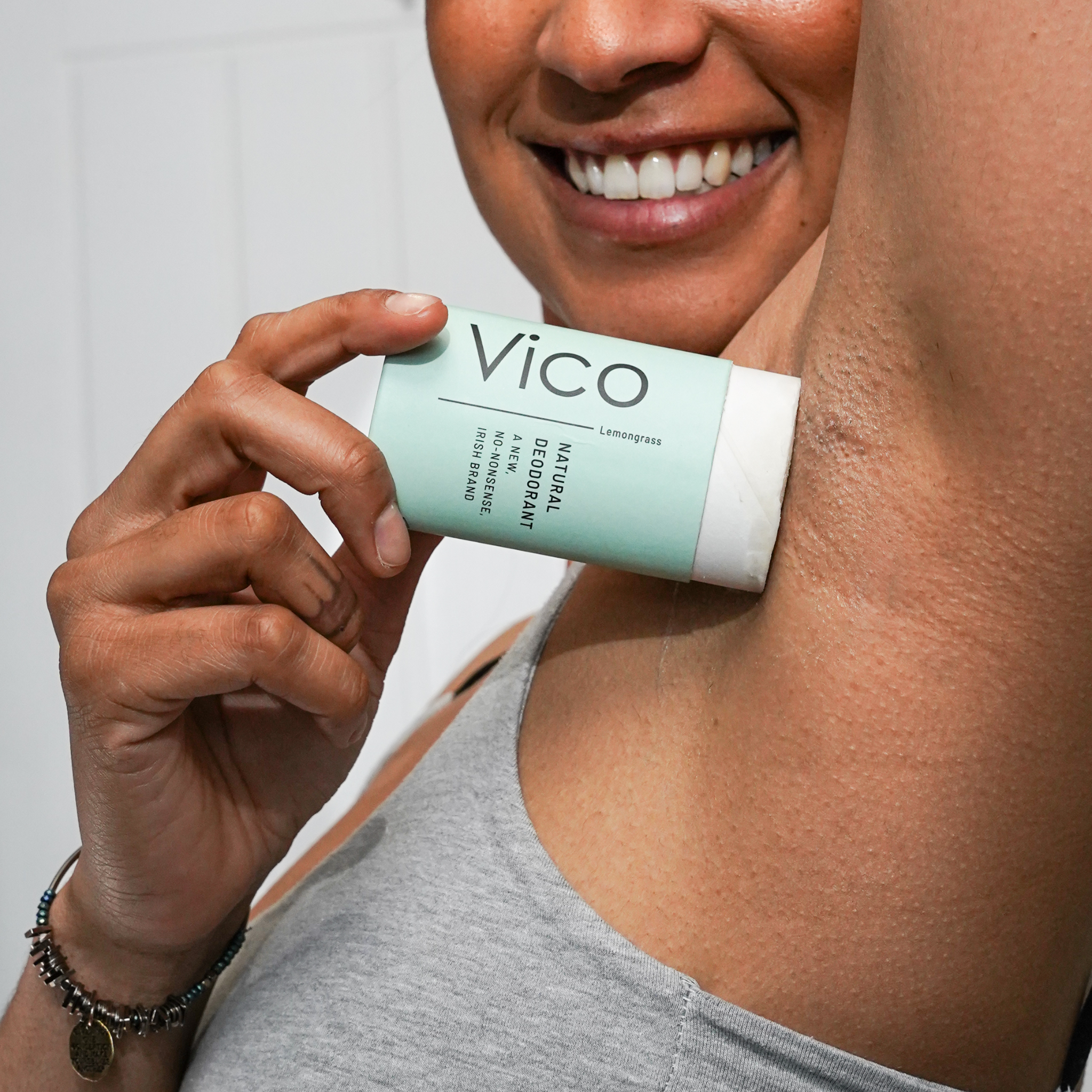 A smiling person applies a stick of Vico natural deodorant to their underarm.