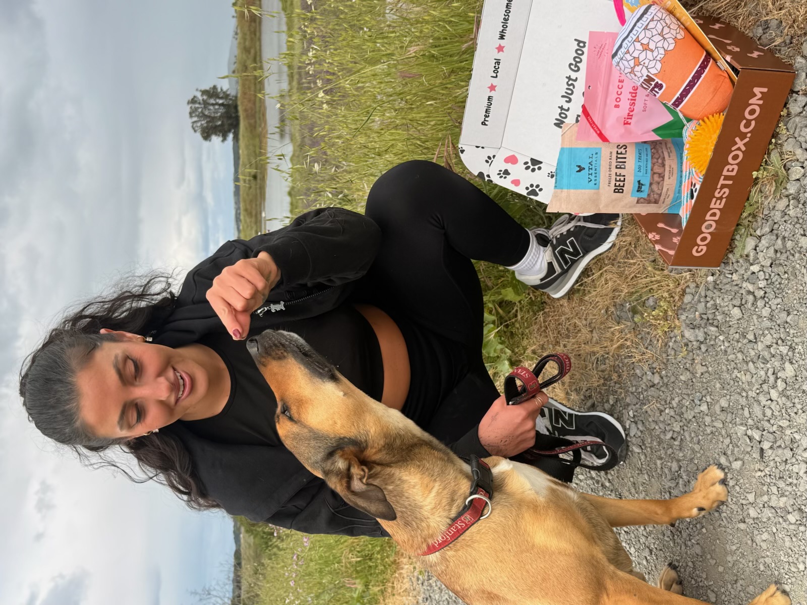 Woman giving treat to dog, with a box of dog products nearby.
