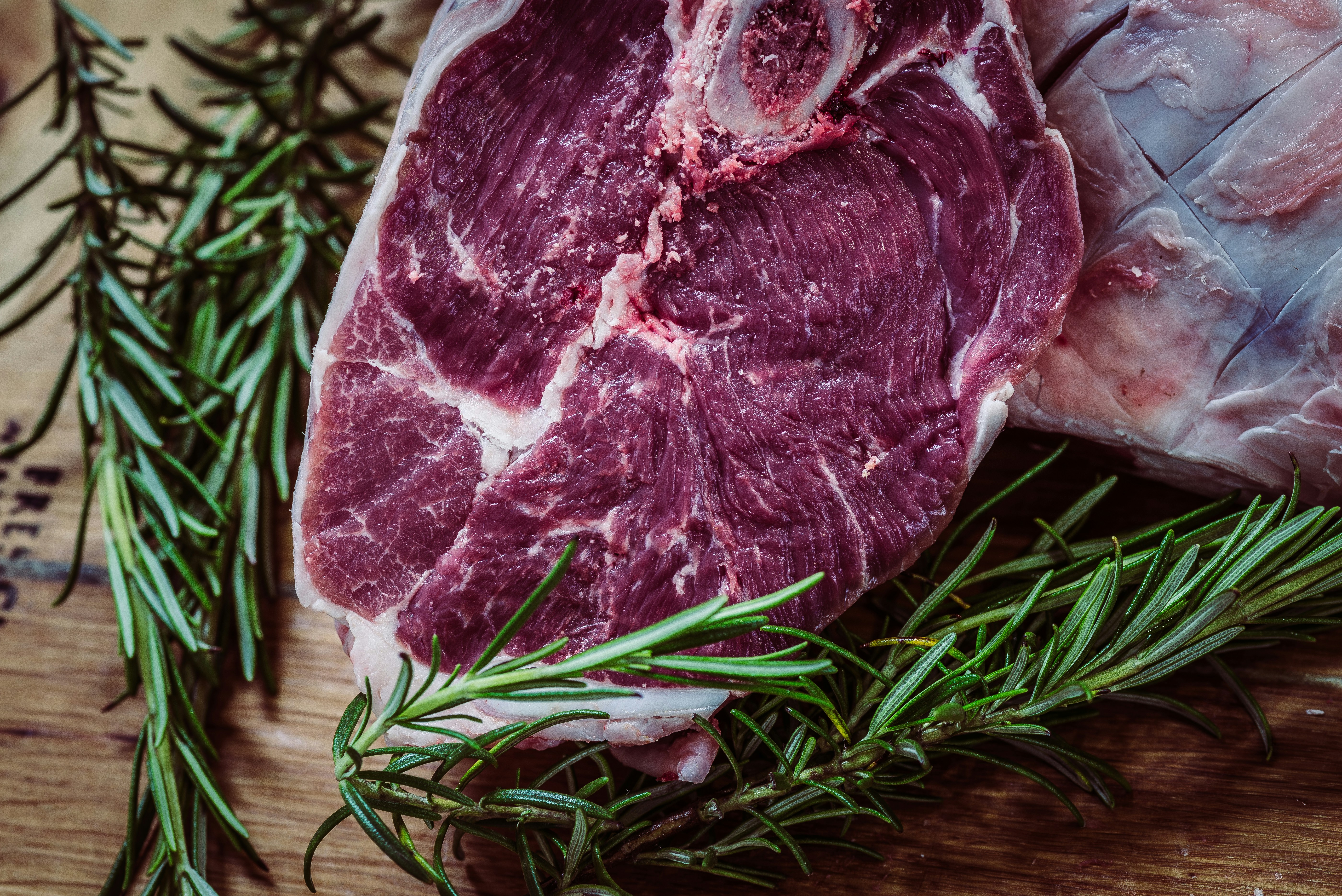 Raw meat slice with rosemary sprigs on a wooden surface.