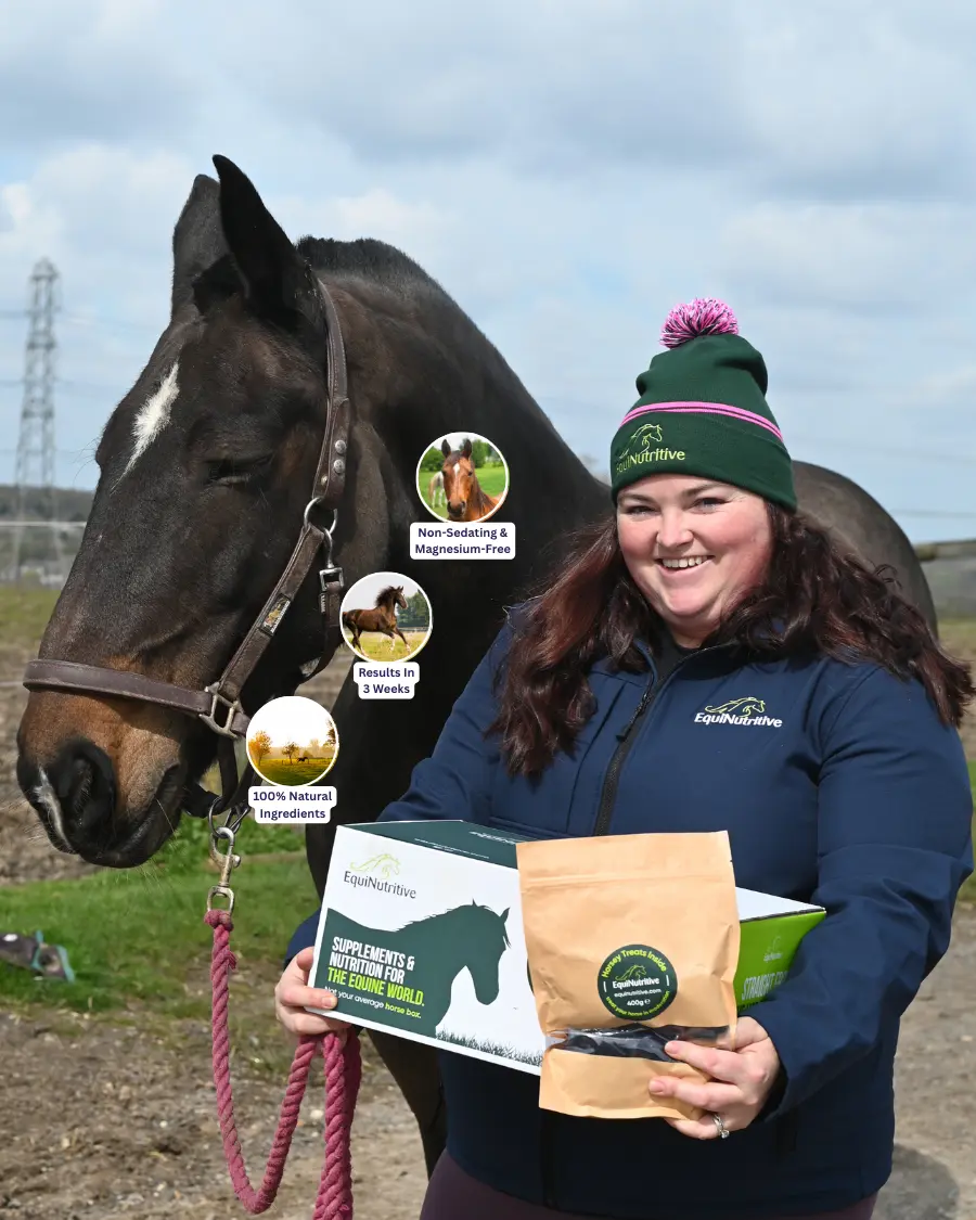 Woman holding equine supplements box and bag, standing beside a horse outdoors.
