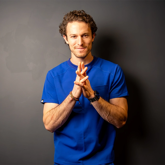 Person in a blue shirt clasping hands against a dark gray background.