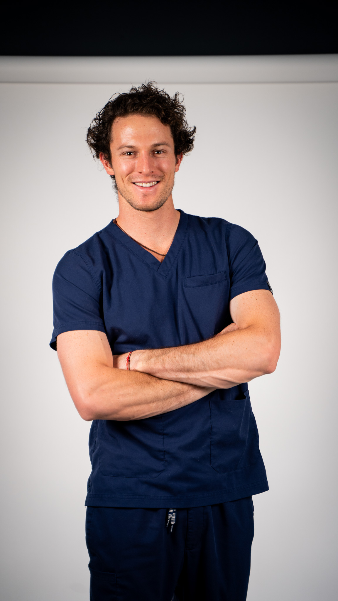 Person in blue scrubs smiling with arms crossed.