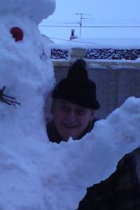 Person standing next to a large snowman in a snowy yard.