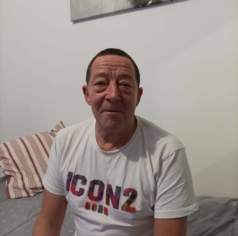A person sitting on a bed wearing a white 'ICON 2' t-shirt.