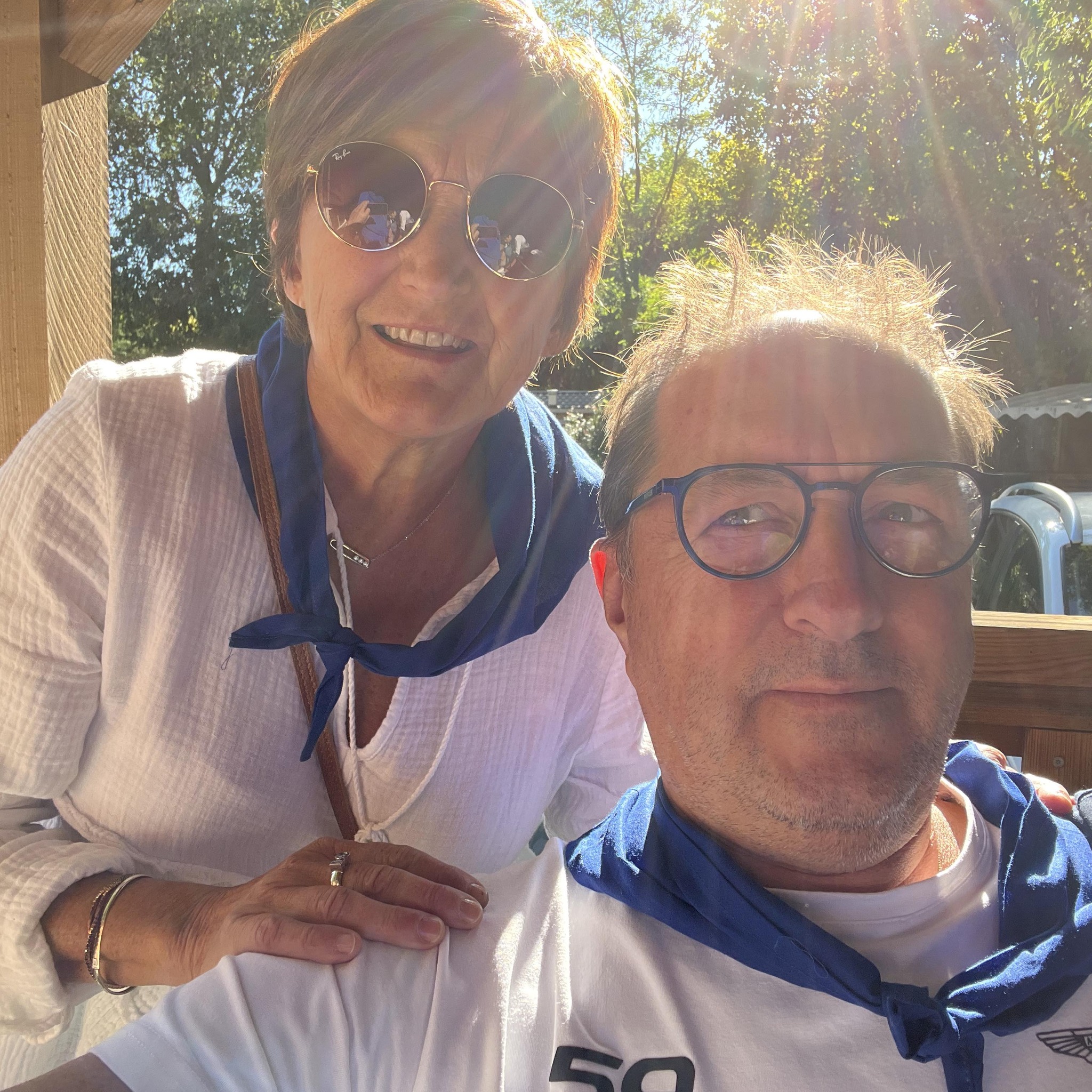 Two people smiling outdoors, wearing blue bandanas in sunny weather.