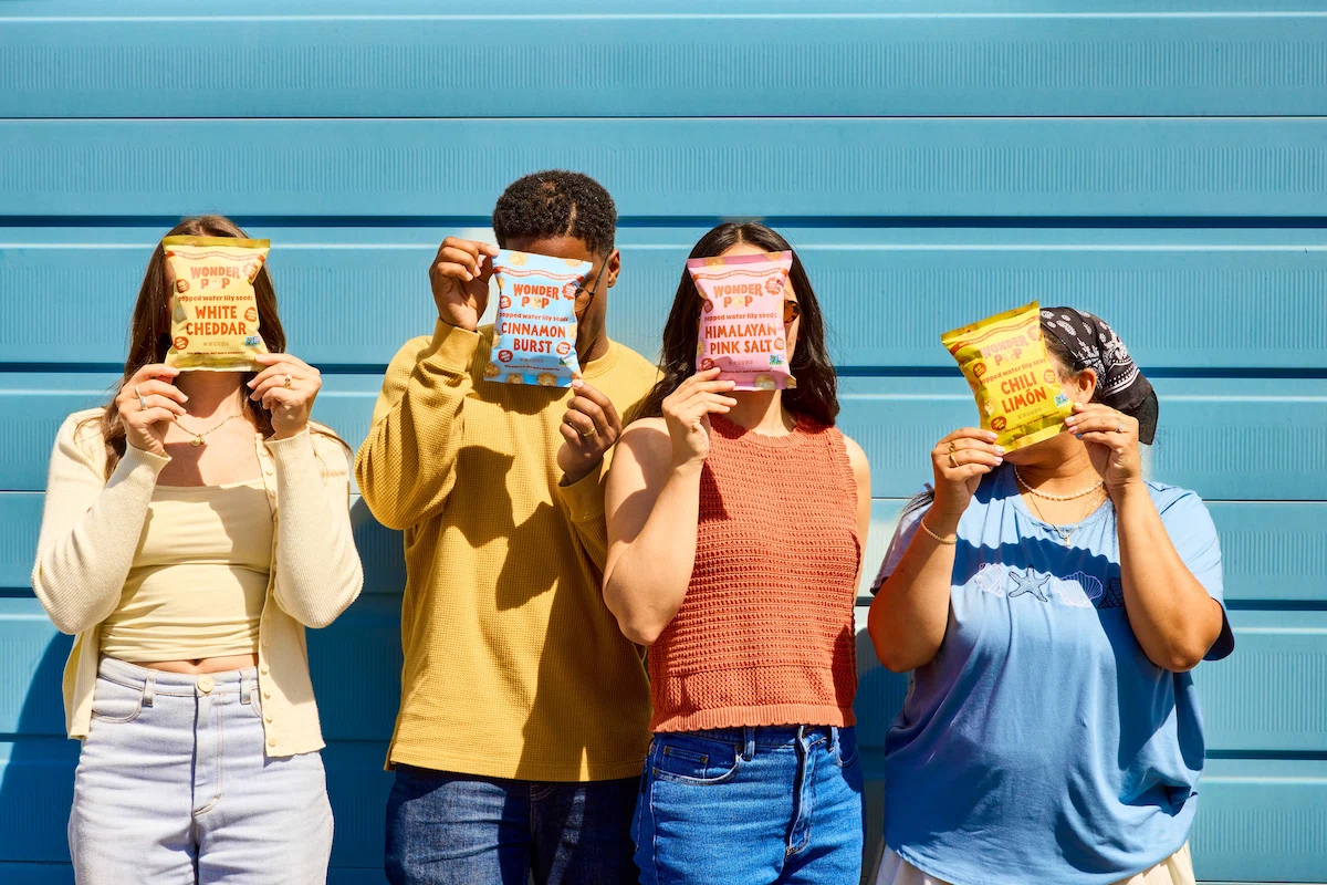 Group of people holding WonderPop snack bags in front of their faces against a blue background