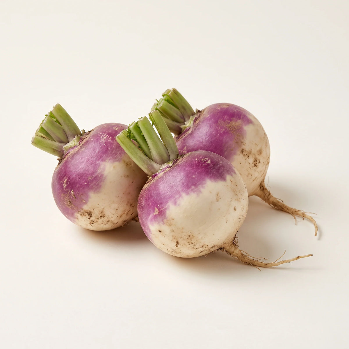 Three fresh turnips with purple tops, green stems, and roots, clustered on a white background.