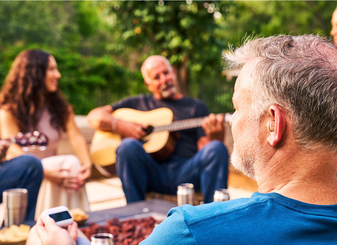 Group gathered outdoors, man playing guitar, others listening.
