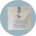 A pouch of Rae Wellness Bone Broth Protein Mix set against a circular blue background.