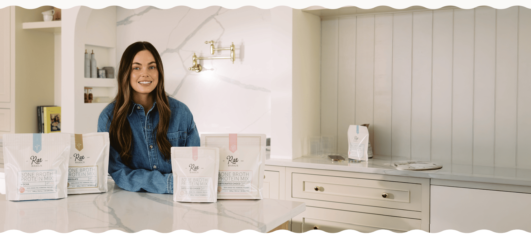 Skotie Rae, founder of Rae Basics, smiling behind pouches of bone broth hot chocolate on a kitchen counter