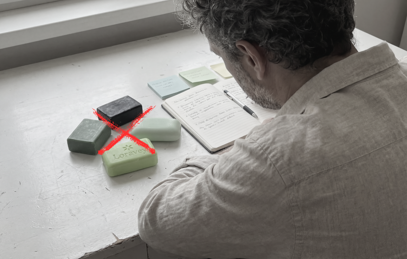 A man writes at a desk with several bars of soap crossed out with a large red X.