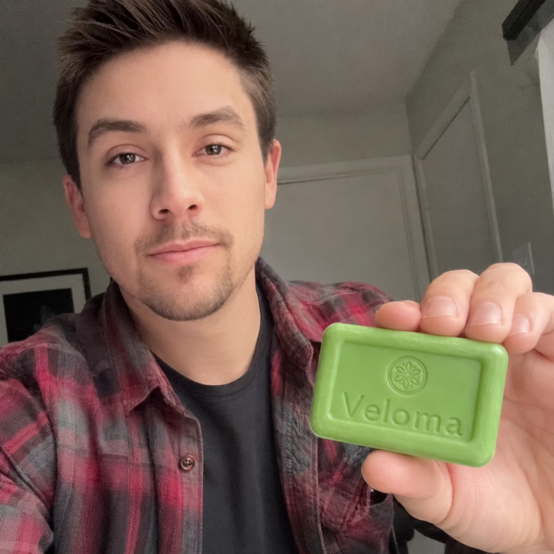 Man in a red and black plaid shirt holds up a bar of Veloma soap