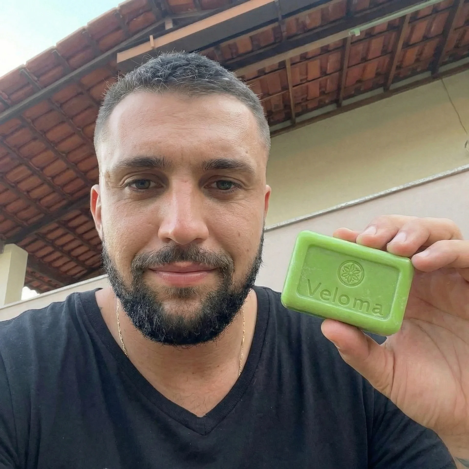A man with a short haircut and beard holds up a green bar of soap with the word Veloma.