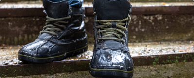 A close-up of a person's wet, black boots with green laces on outdoor steps.