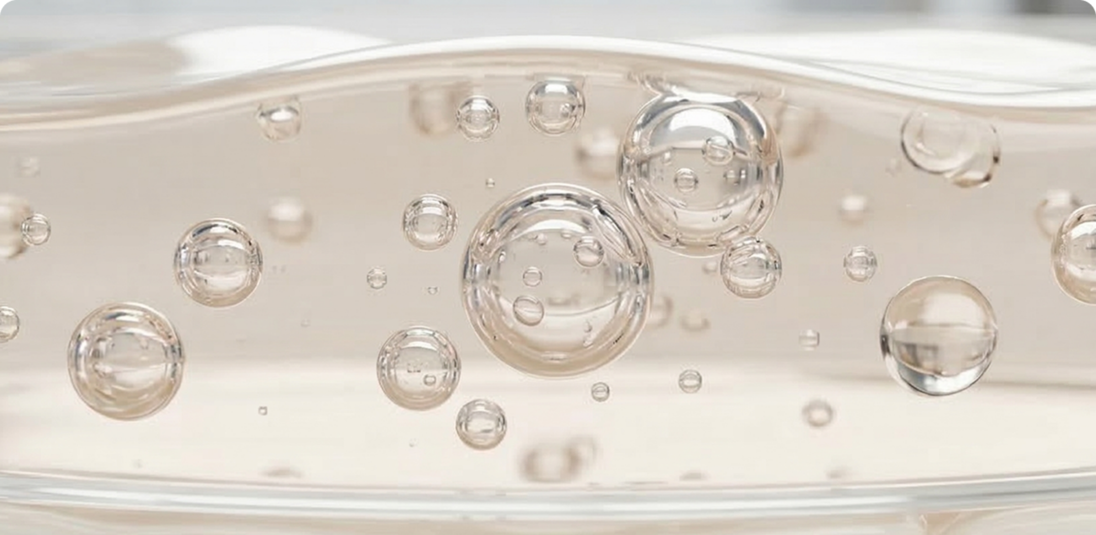 A close-up, macro view of clear bubbles of various sizes suspended in a light-colored liquid.