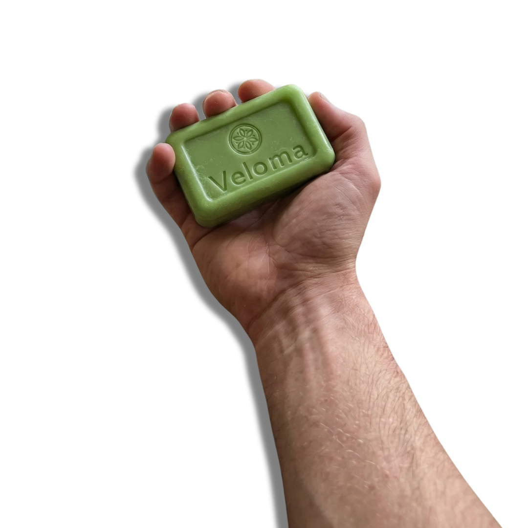 A hand holding a green bar of Veloma soap against a black background.