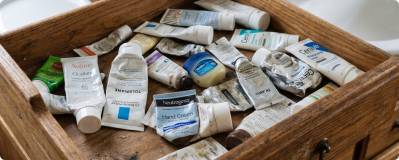 A cluttered wooden drawer filled with used and squeezed tubes of lotions and creams.