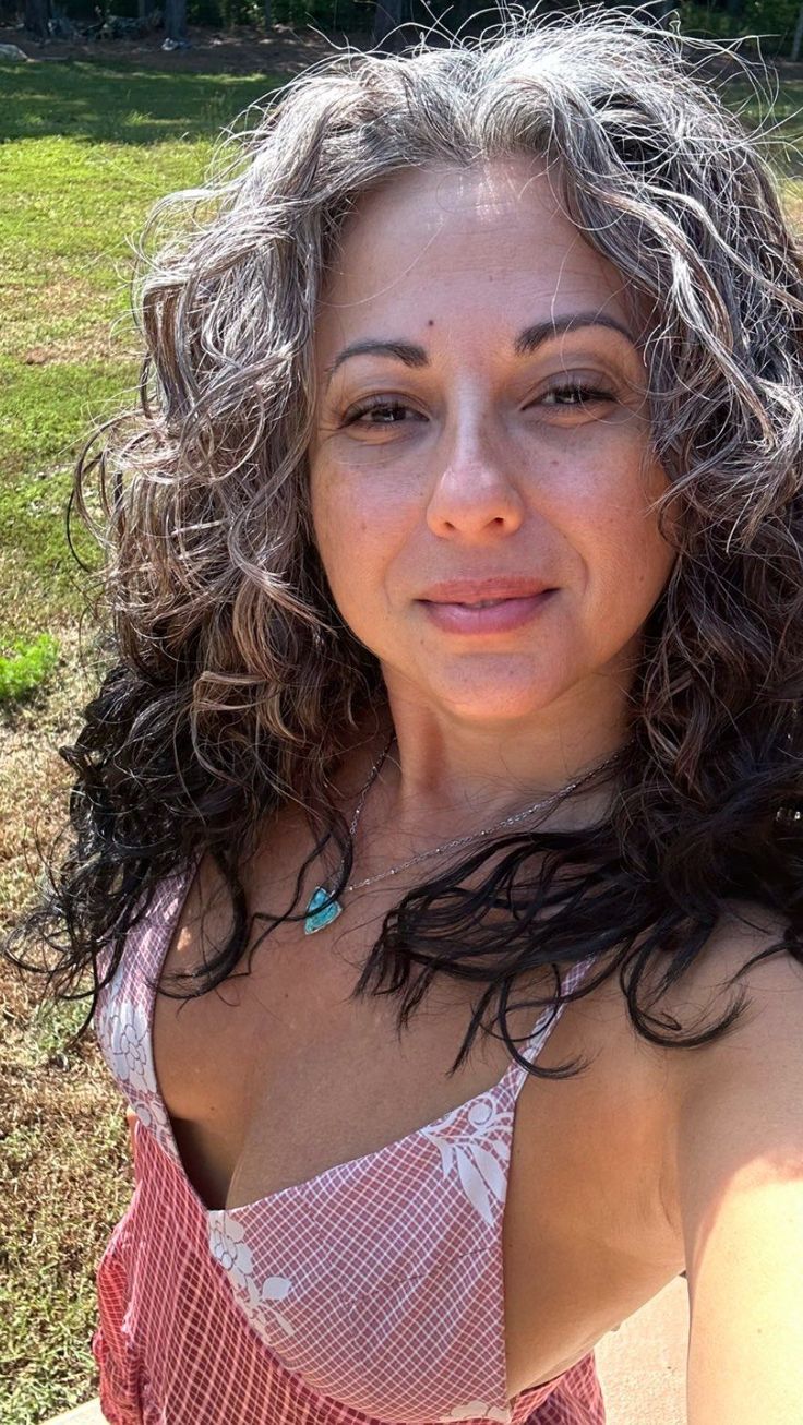 Person with curly hair outside wearing a patterned dress and necklace.