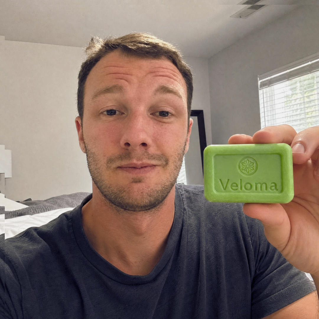 Man in a grey t-shirt holds up a bar of soap that says Veloma