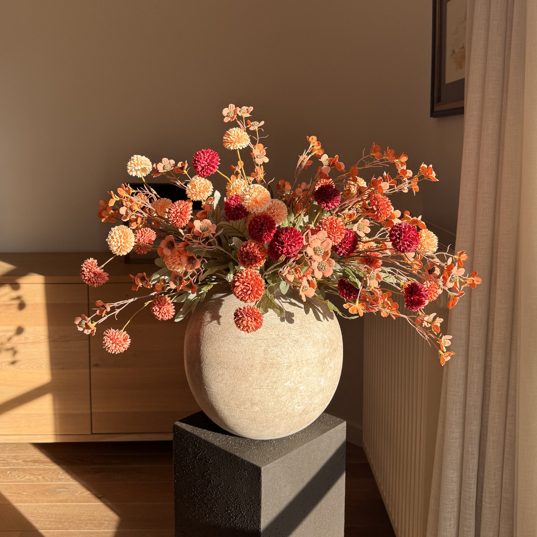 A large bouquet of red and orange flowers in a round, stone-like vase on a pedestal.