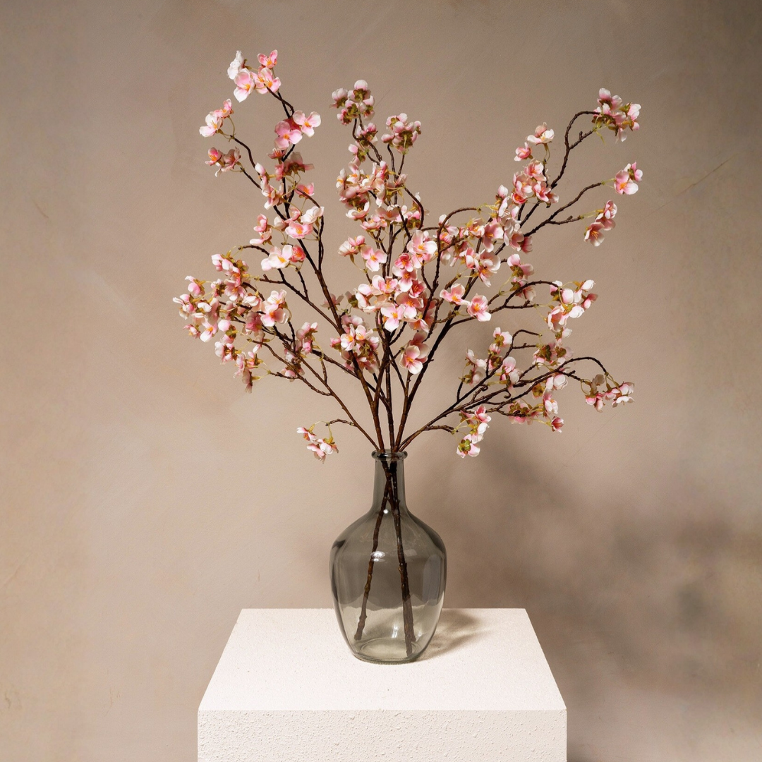 A glass vase with pink cherry blossoms on a white pedestal.