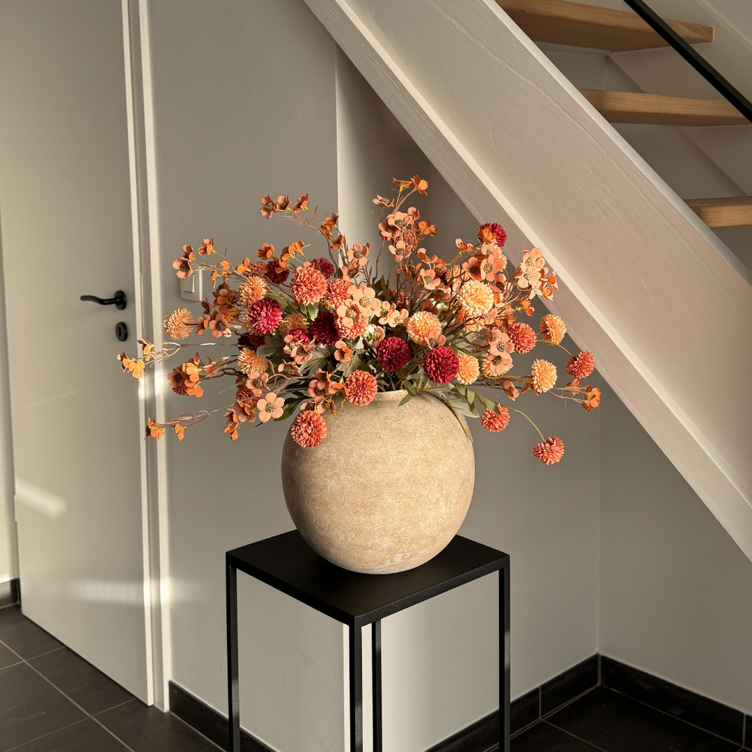 A bouquet of orange and red flowers in a round, textured vase on a small black table.
