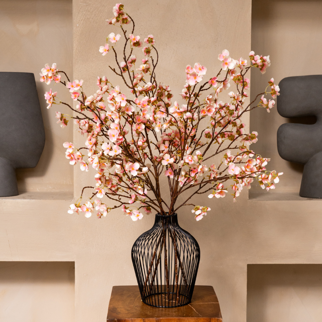 Pink cherry blossoms in a black wire vase on a wooden table.