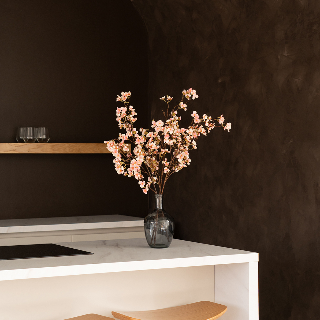 Vase with pink flowers on a marble countertop, dark wall background.