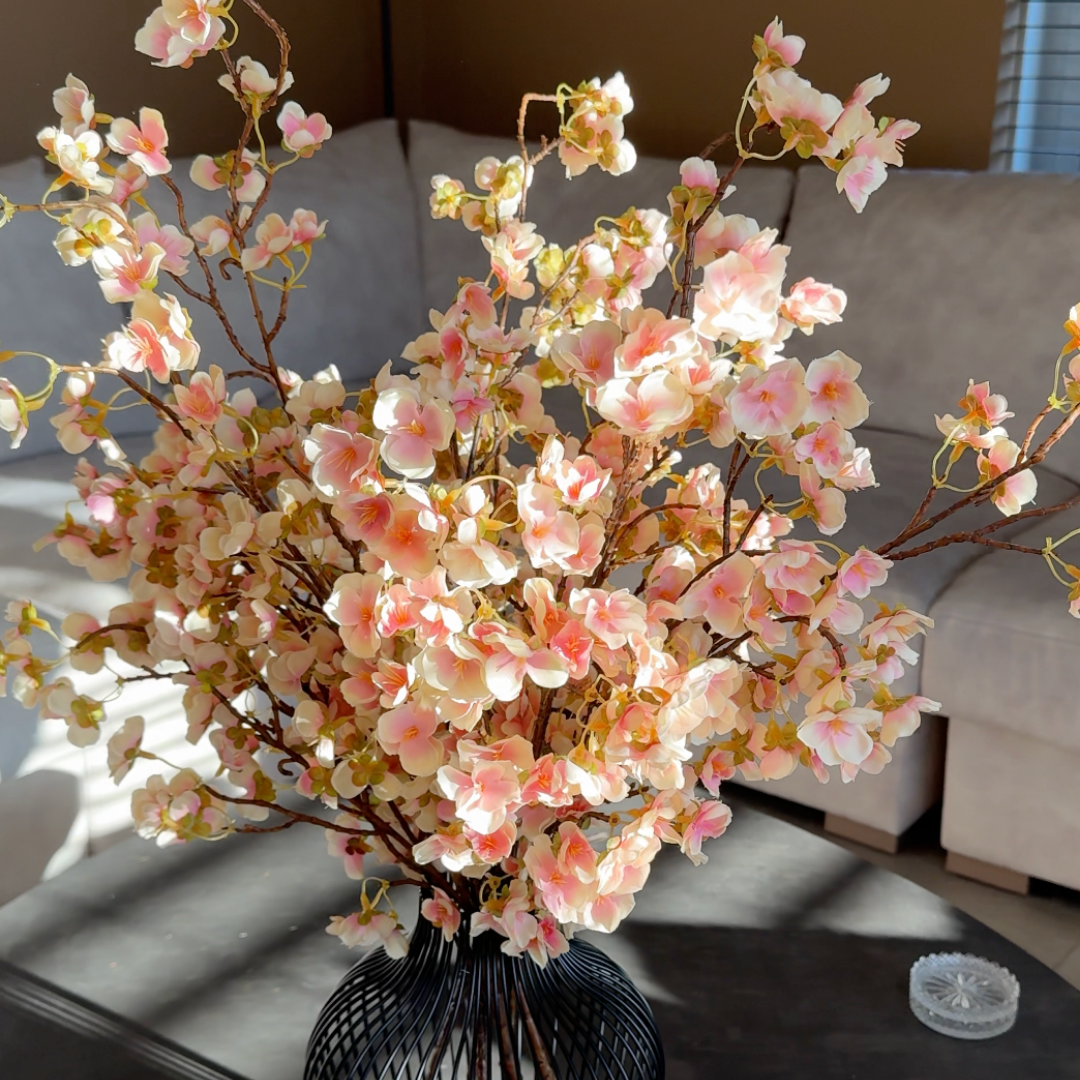 A bouquet of pink and white cherry blossoms in a black wire vase on a table.