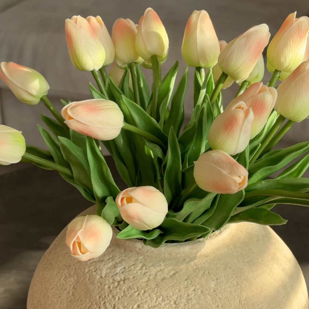 A bouquet of artificial cream and pink tulips in a textured, light-colored vase.