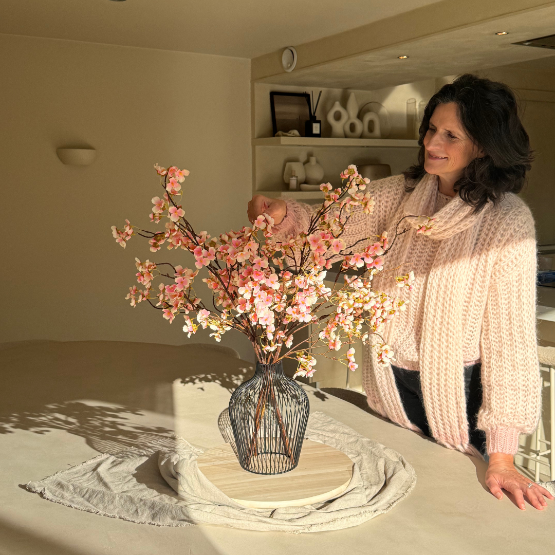Person arranging pink flowers in a vase on a table.