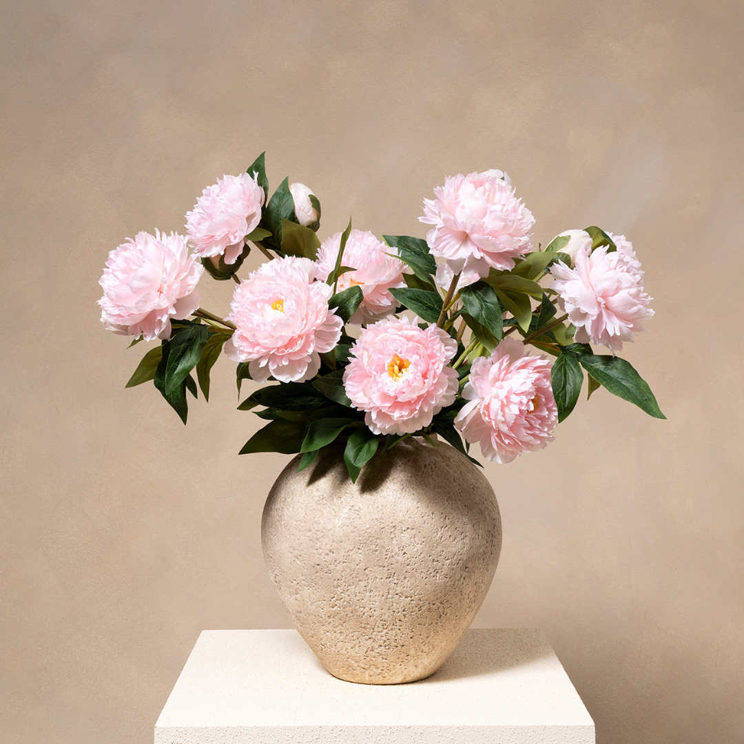 Pink peonies in a beige textured vase on a pedestal.