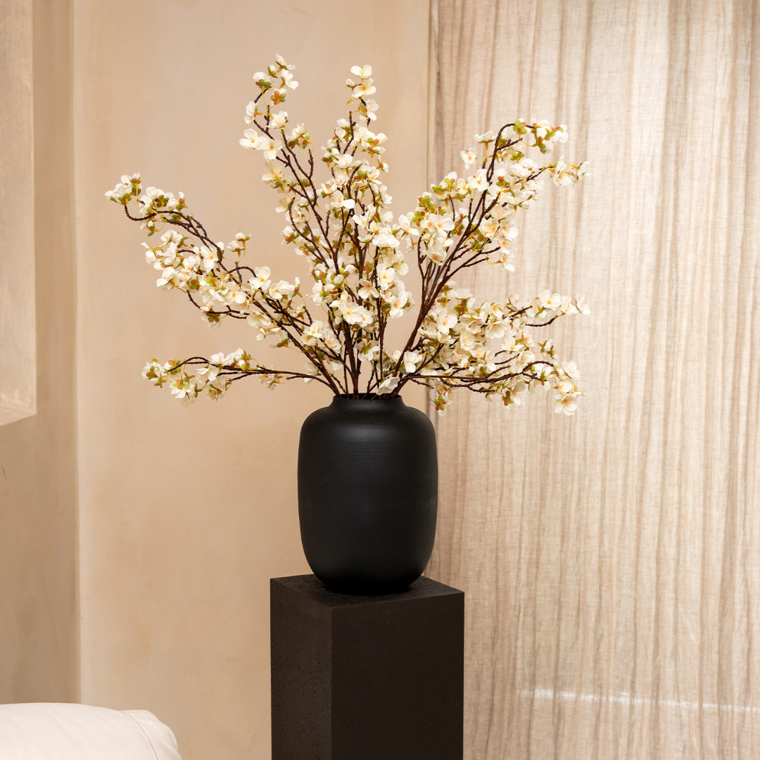 Black vase with white blossoming branches on a pedestal.