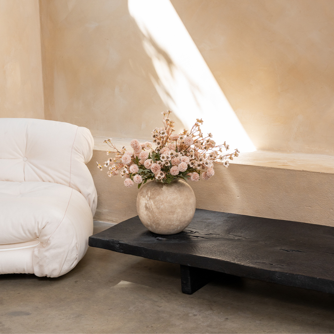 Vase with flowers on dark wooden table beside a white couch.