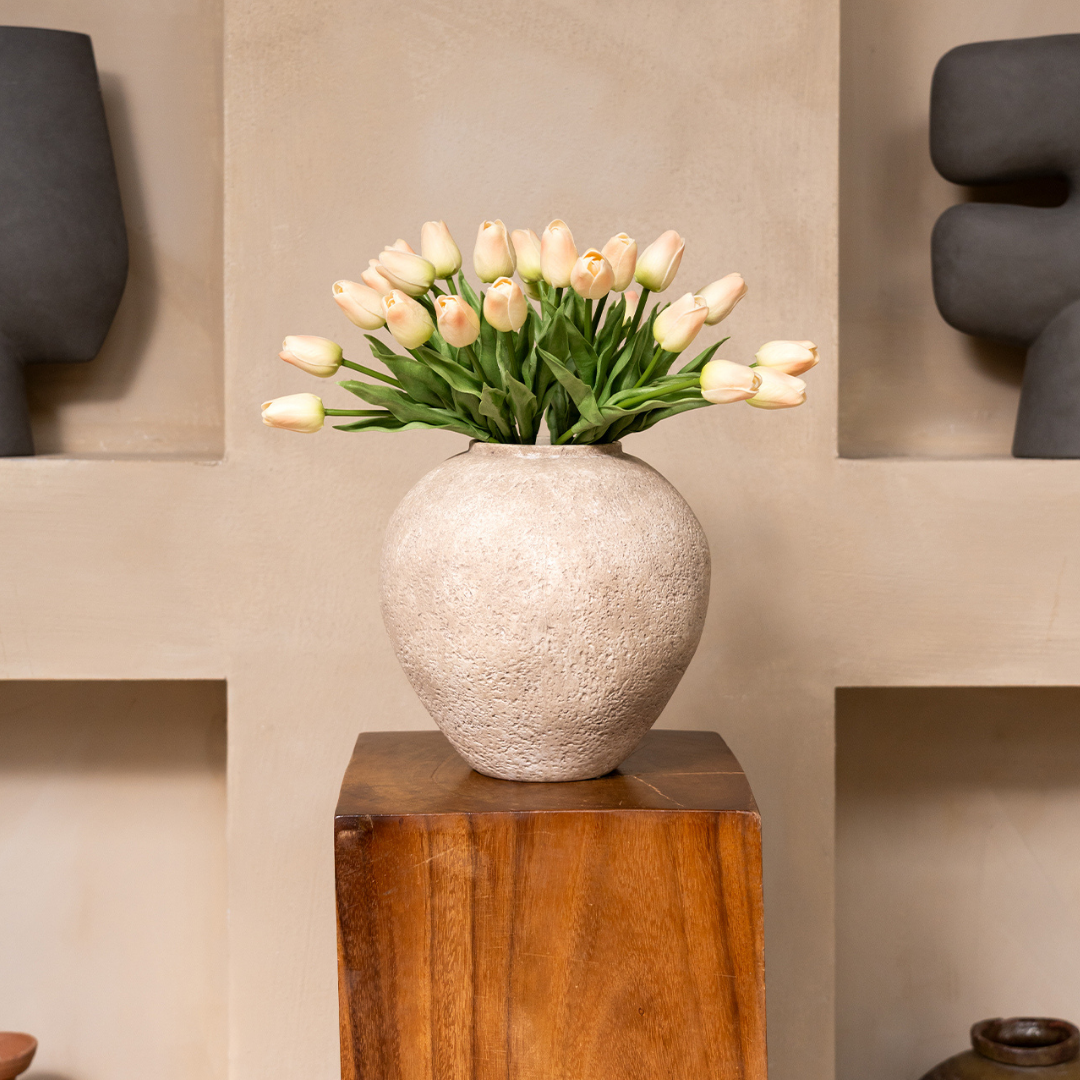 Beige vase with white tulips on a wooden pedestal.