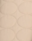 A close-up of light beige quilted fabric with a repeating oval pattern.
