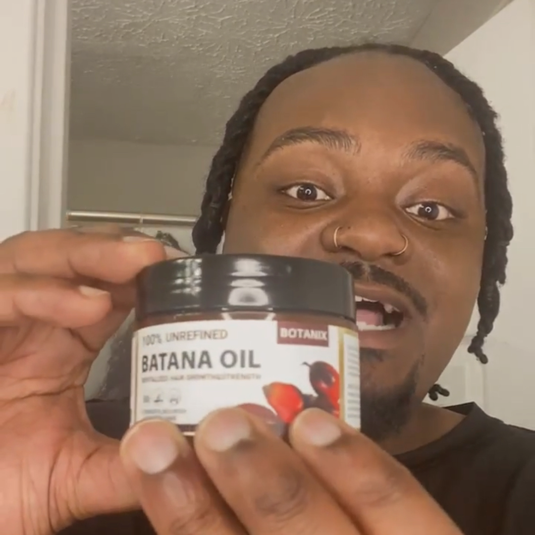 Person holding a jar of 100% unrefined Batana oil.