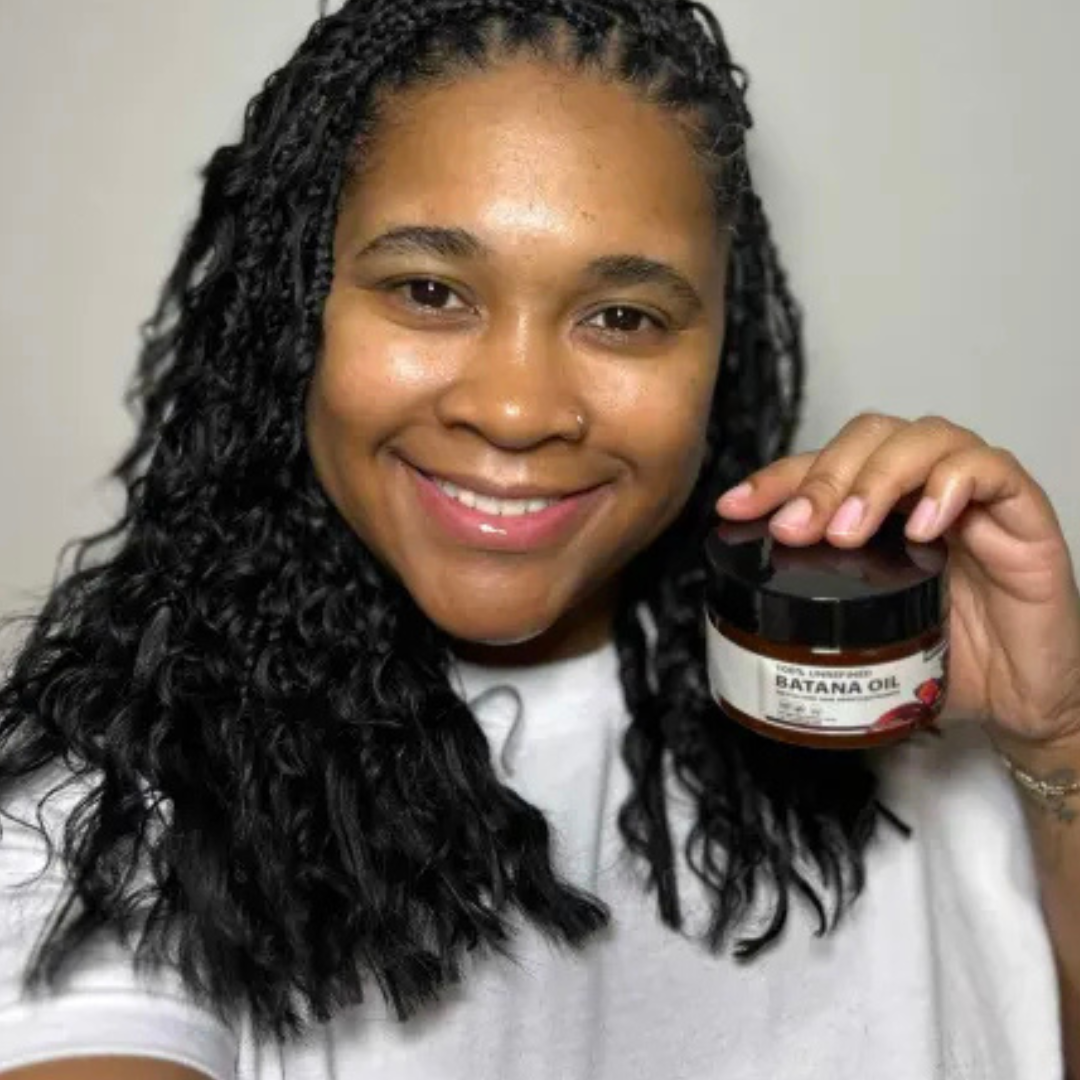 Person smiling and holding a container labeled 'Batana Oil.'