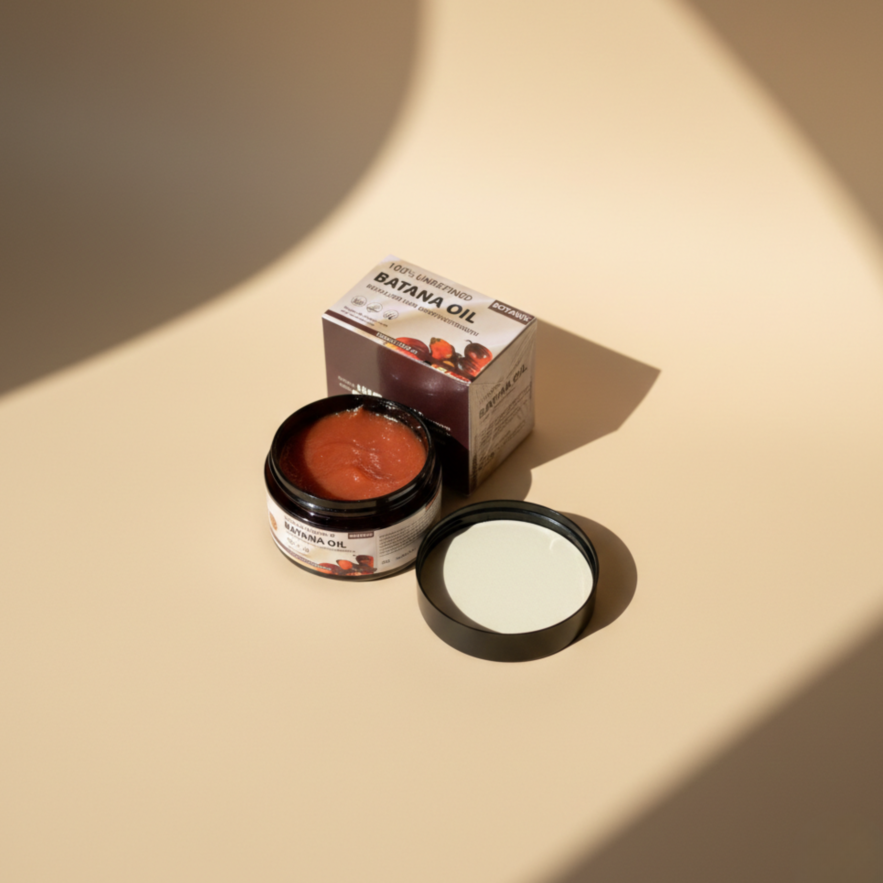 An open jar of Batana Oil sits next to its box on a beige surface with soft shadows.