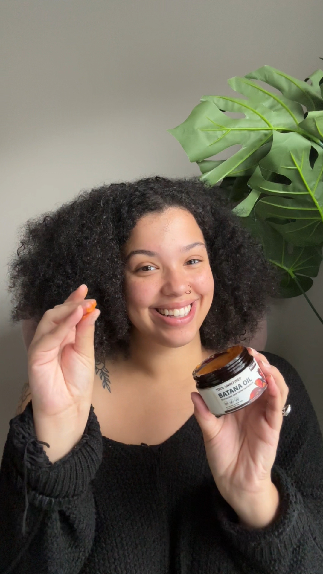 Smiling person holding a jar of Batana oil and a small amount in hand.