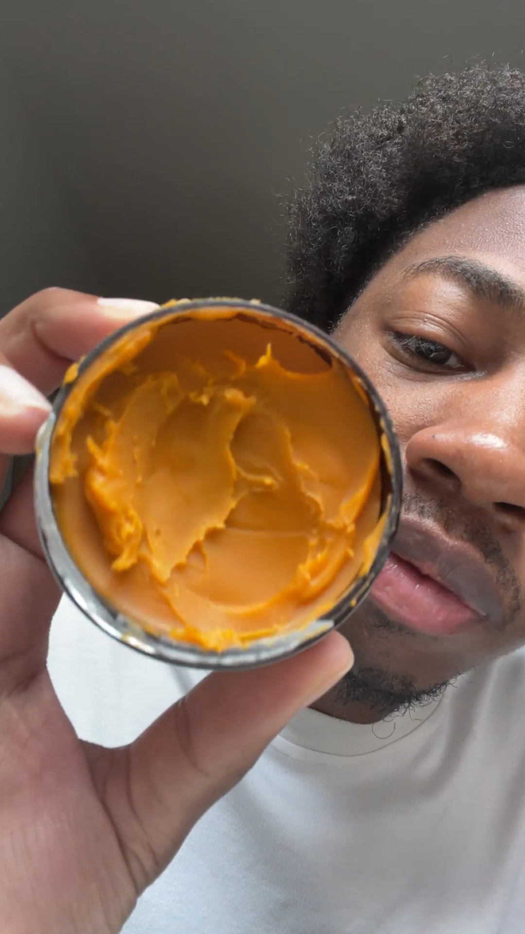 Person holding a container of orange buttercream, close-up view.