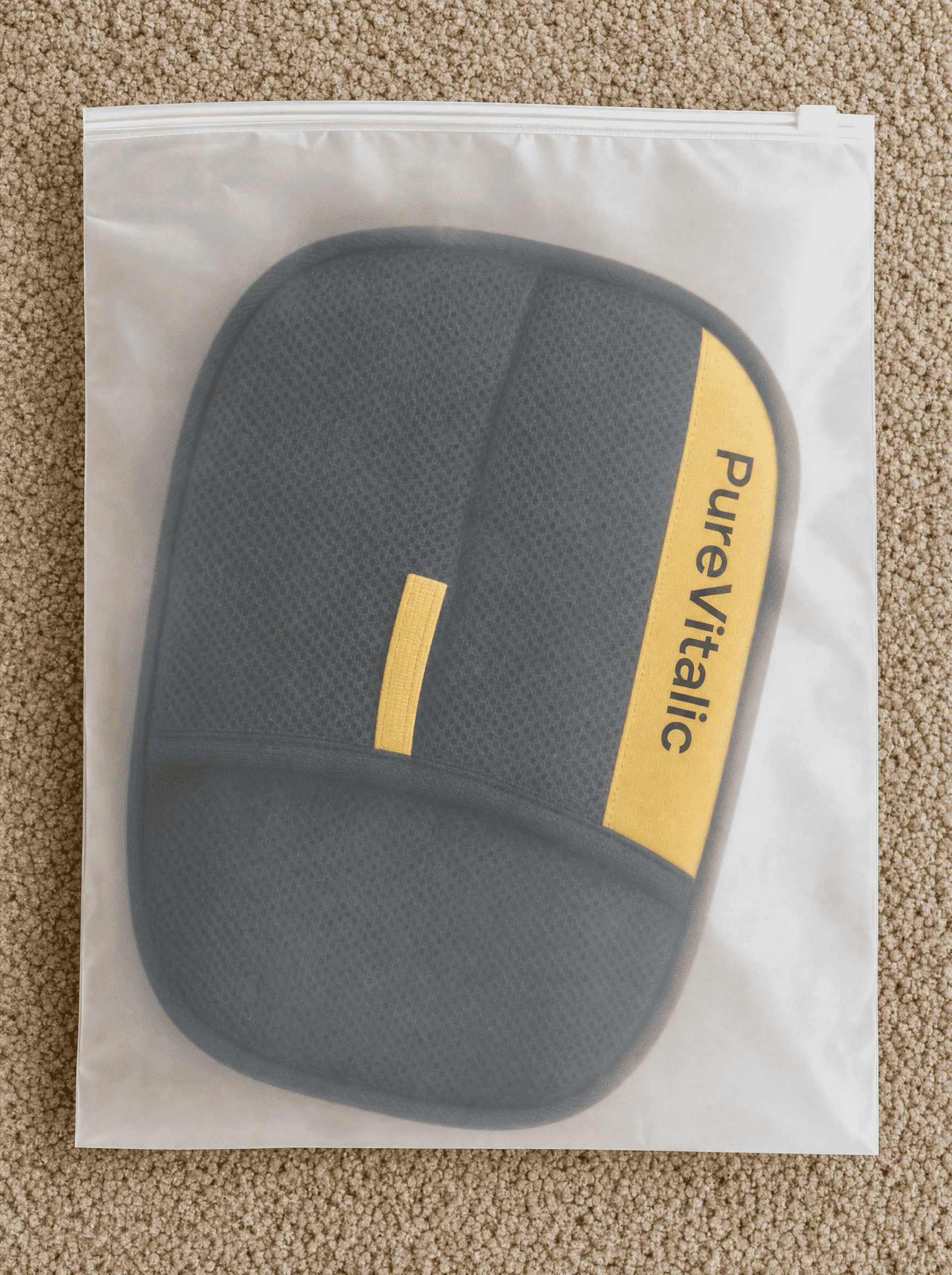 A gray padded item with a yellow 'PureVitalic' brand stripe inside a plastic zip-top bag on carpet.